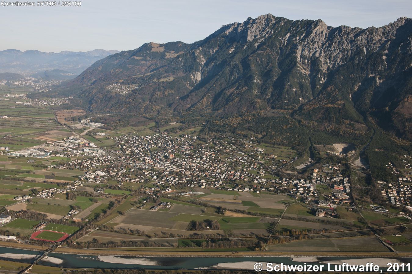 Liechtensteiner Rheintal, Schaan (Position 2'757'154.67, 1'226'027.41) im Bildzentrum. Blick nordwärts. Maiensäss am Hang (Bildmitte): Planken, darunter gelegen im Tal: Nendeln. weiter nordwärts: Mauren. Am linken Bildrand oben: Eschen.